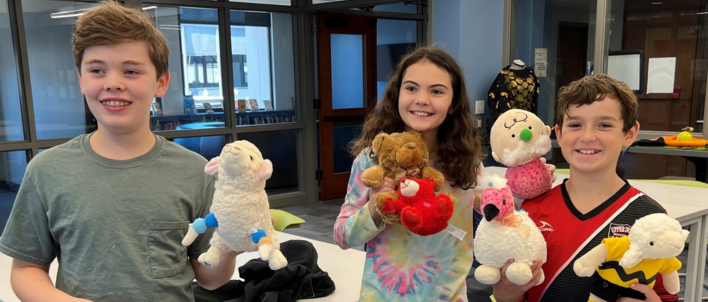 Three children pose holding stuffed animals that they made during a library program