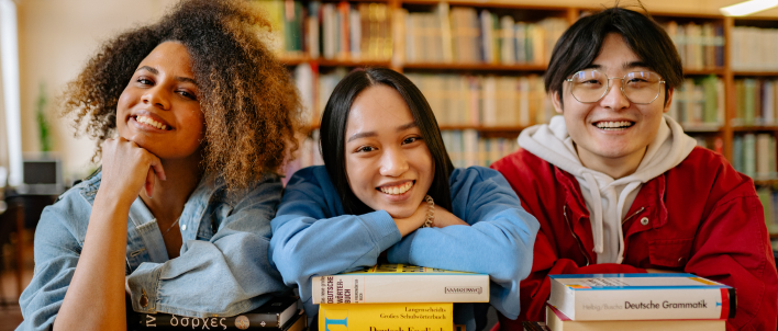 Three teenagers pose with books in front of a bookcase